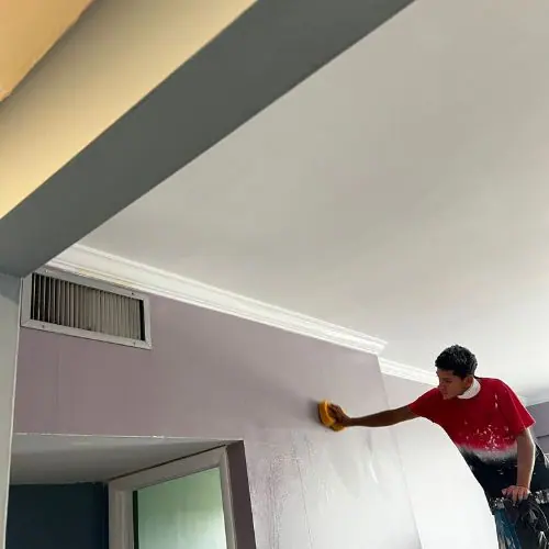 Painter cleaning crown molding and walls from a ladder